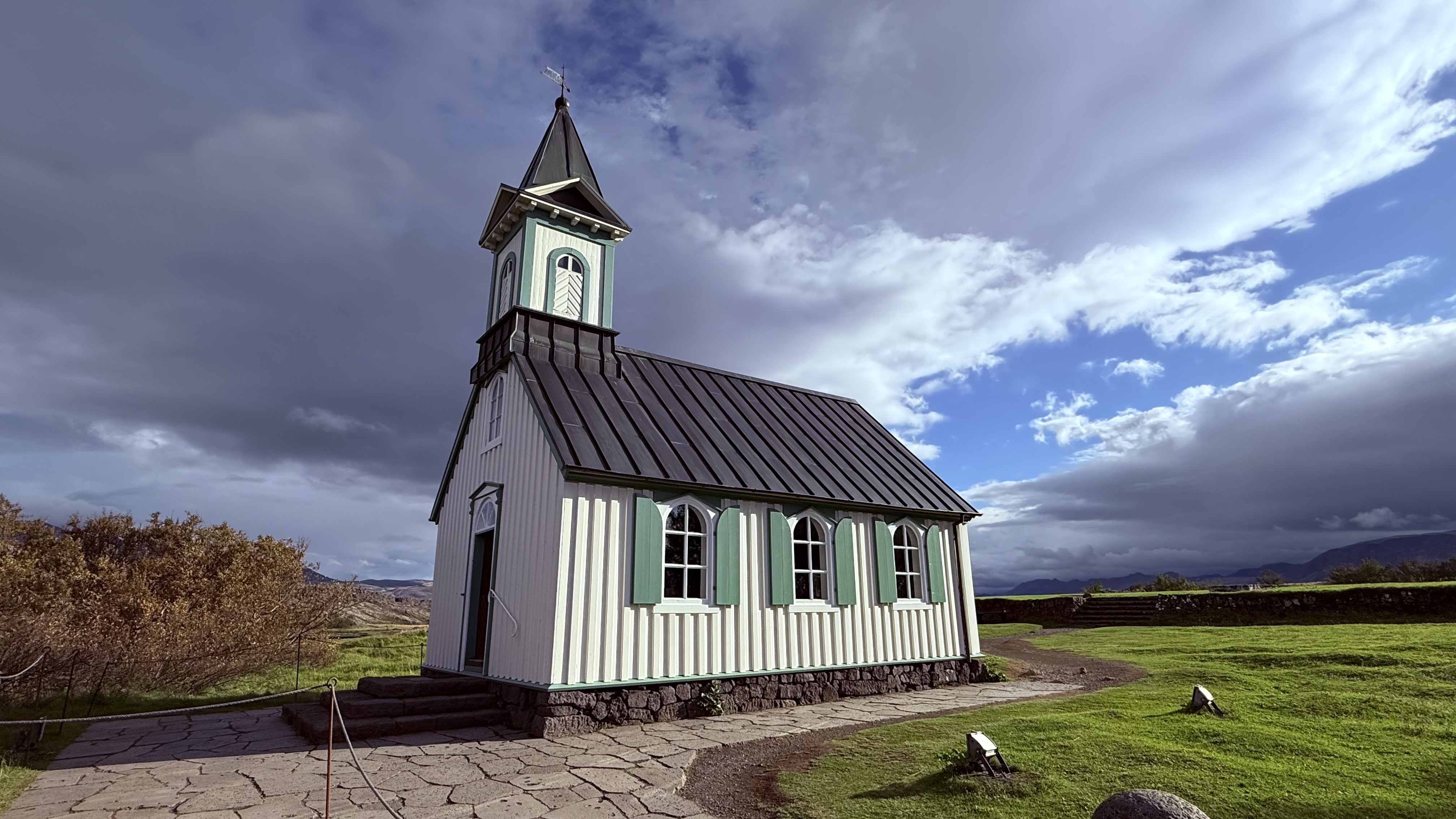 A small Icelandic church in a green field under dramatic clouds at Thingvellir