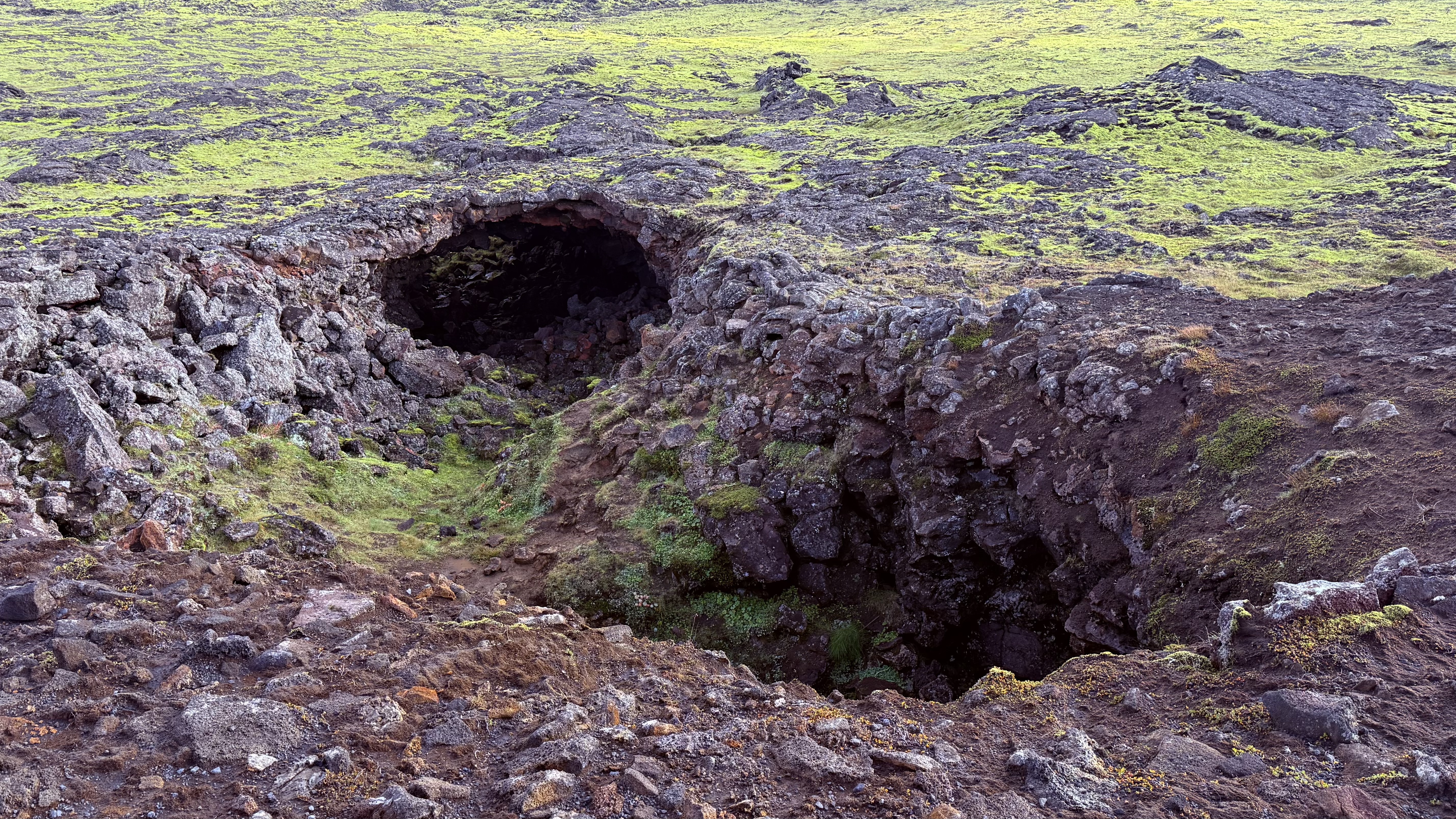 A lava cave entrance surrounded by moss-covered volcanic rock