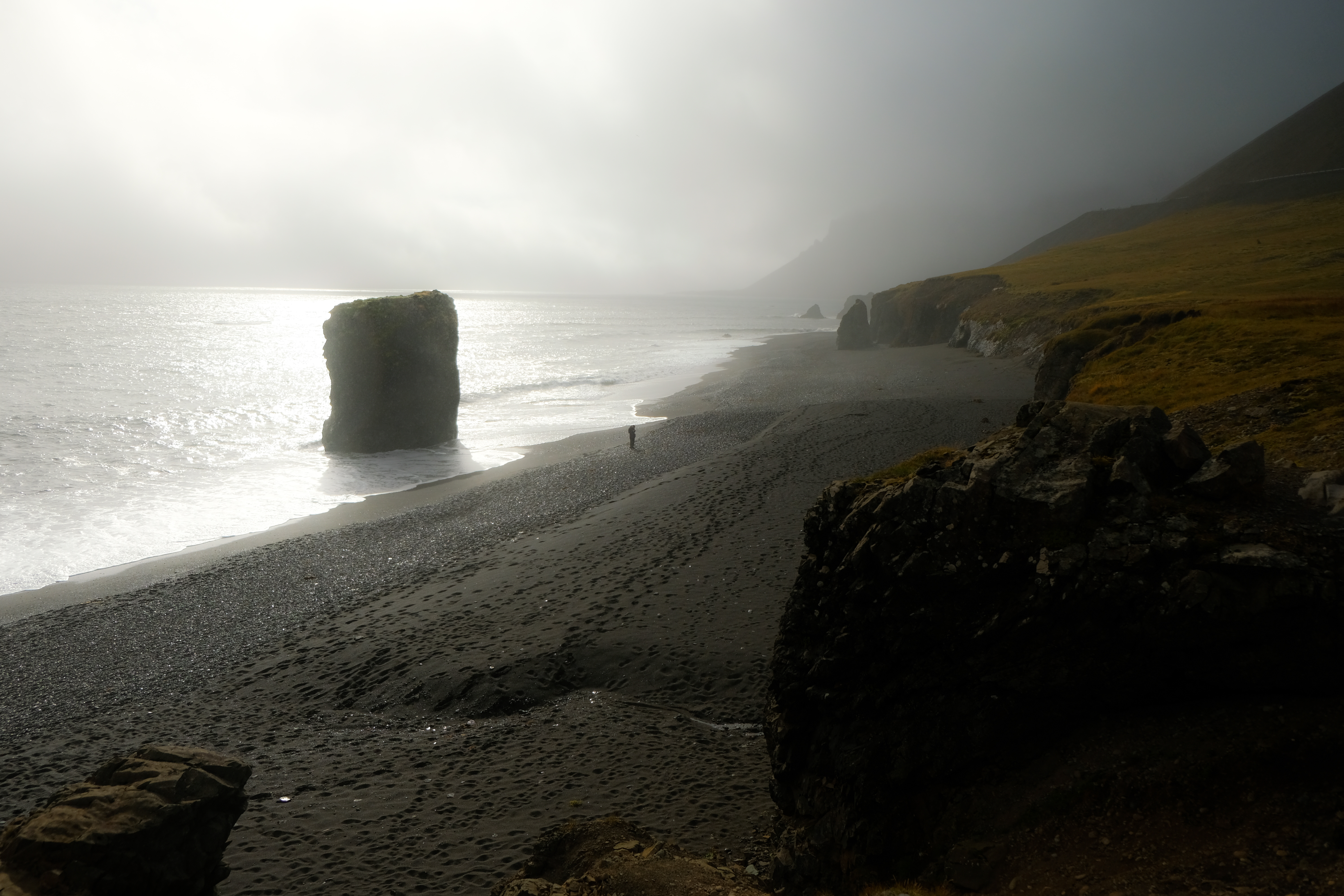 Misty black beach with lone sea stack and a solitary figure